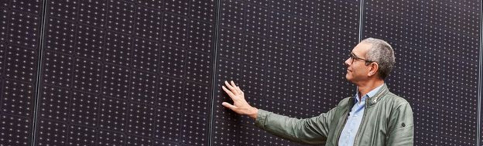Ein Mann begutachtet horizontal angebrachte Solarmodule. Mit einer Hand streicht er über ein Panel.